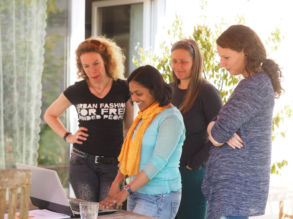 Auf diesem Foto steht eine Gruppe hinter Krishna-Sara Helmle. Sie schauen auf einen Laptop, der vor ihnen auf einem Tisch steht.