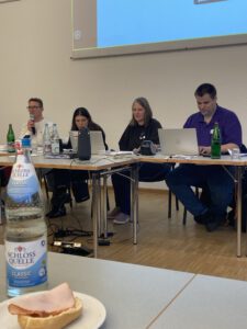 Vier Personen sitzen an einem Tisch. Zwei davon haben einen Laptop aufgeklappt und schauen auf die Bildschirme. Es handelt sich um Mitglieder des Vorstands des Netzwerks Leichte Sprache.